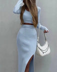 Woman in a light blue outfit holding a white handbag against a plain background