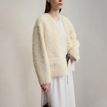 Woman wearing a light beige fluffy cardigan over a white dress against a plain background