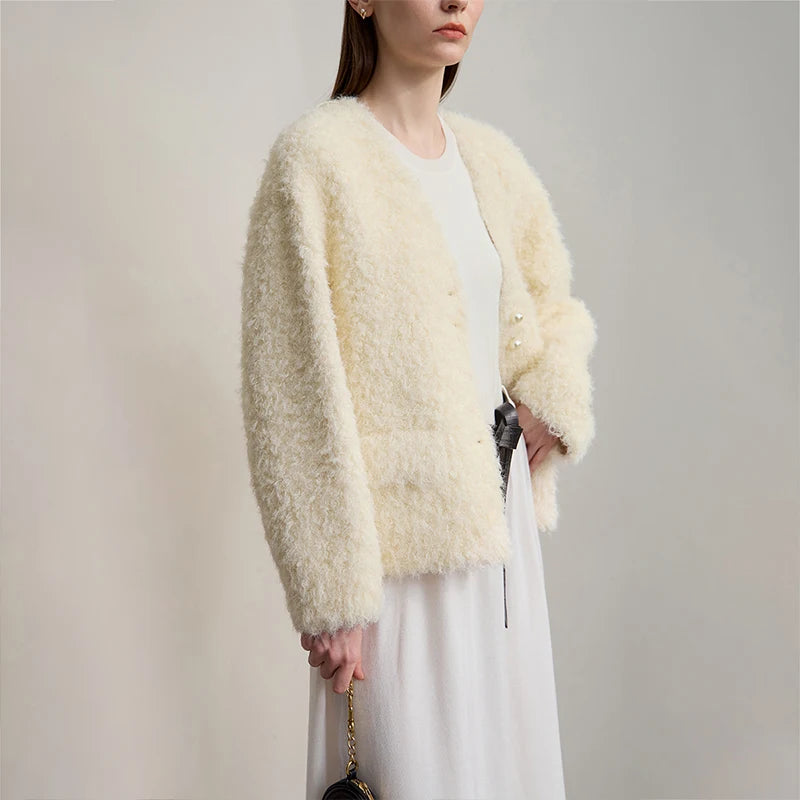 Woman wearing a light beige fluffy cardigan over a white dress against a plain background