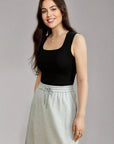 Woman wearing a black tank top and gray skirt against a plain background