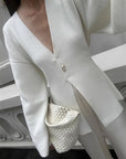 Person wearing a white blazer holding a small textured handbag indoors.