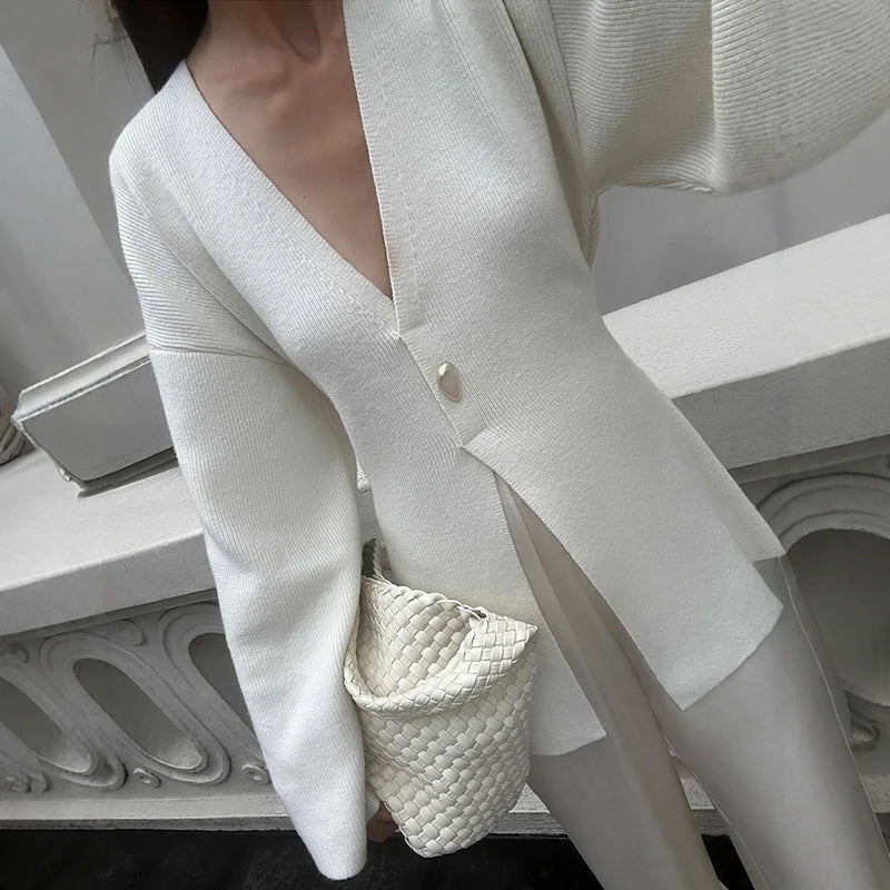 Person wearing a white blazer holding a small textured handbag indoors.