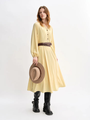 Woman wearing a yellow dress with a brown belt and holding a straw hat on a white background