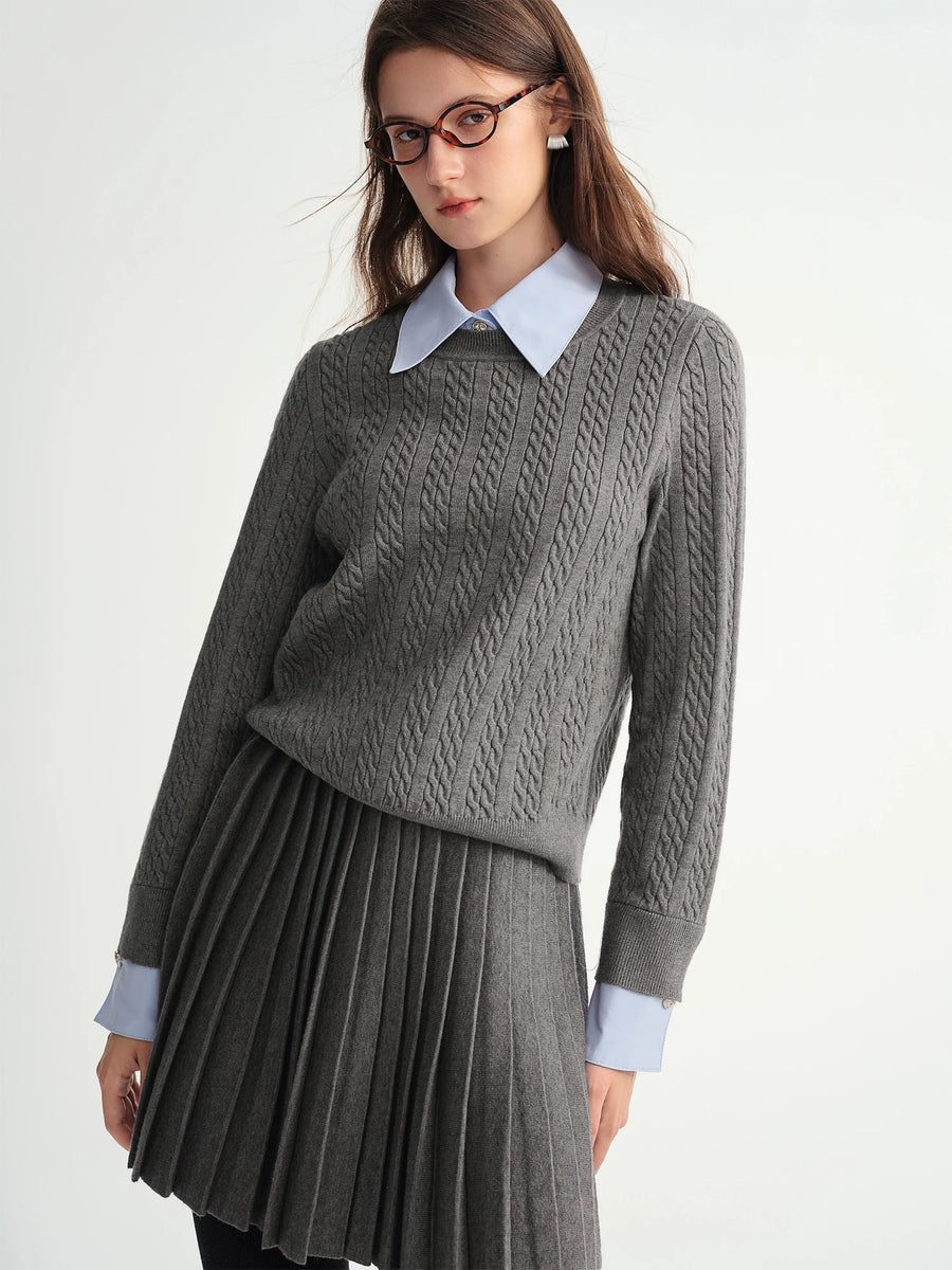 Woman wearing a gray cable knit sweater and pleated skirt with a white shirt collar.