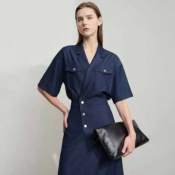 Woman wearing a navy blue dress with a black clutch against a light gray background, featuring the brand 'Amii'.