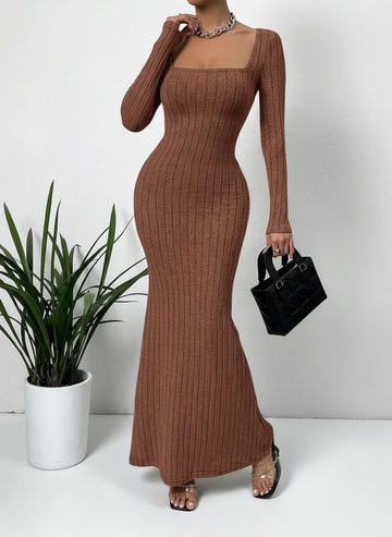 Woman wearing a brown ribbed dress holding a black handbag against a plain background