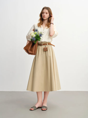 Woman wearing a white blouse, beige skirt, and holding a brown bag with flowers against a white background