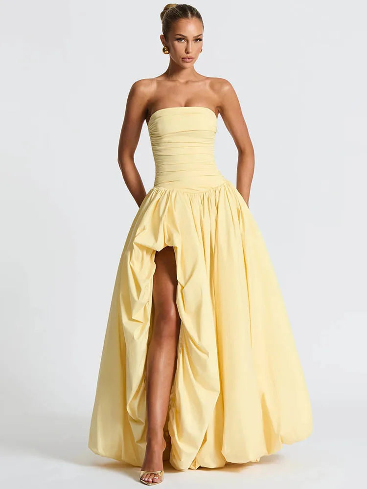 Woman wearing a yellow strapless gown with a high slit on a white background