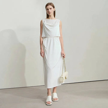 Woman wearing a white dress holding a small handbag on a plain background