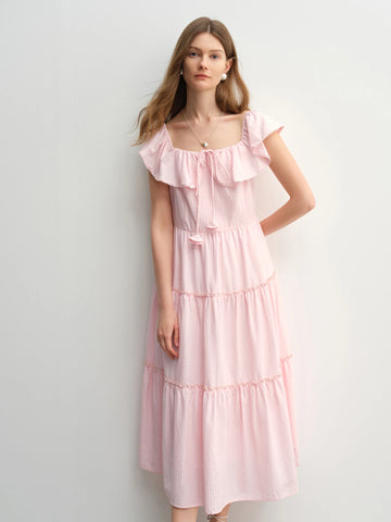 Woman wearing a pink dress with ruffled sleeves against a light gray background