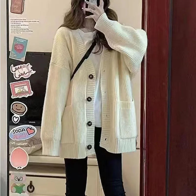 Person wearing a white cardigan taking a mirror selfie.