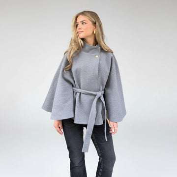 Woman wearing a gray coat standing outdoors near a building.