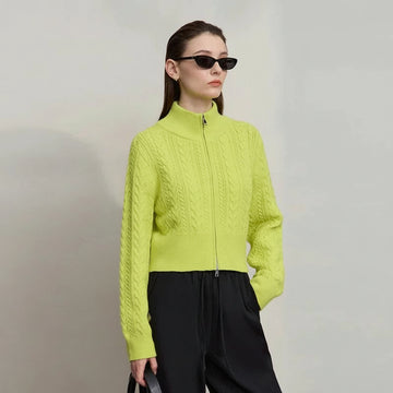Woman wearing a bright green cable knit jacket with a plain background