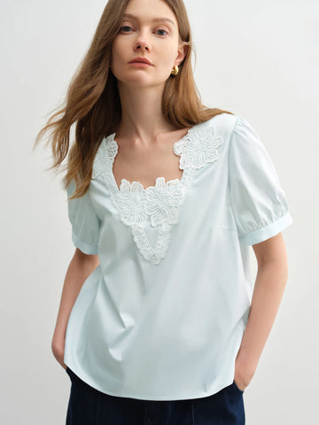 Woman wearing a light blue blouse with white lace details on a plain background
