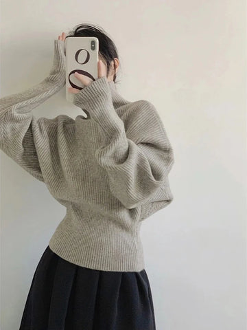 Person wearing a beige sweater and black skirt against a plain background