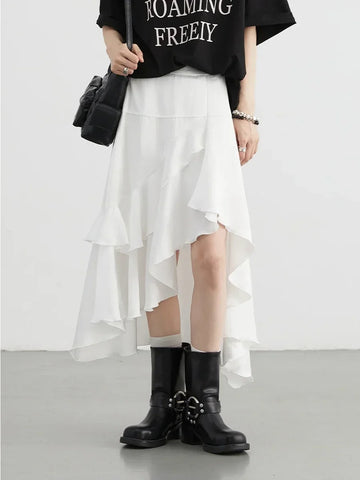Person wearing a black t-shirt with text, white skirt, and black boots on a plain background