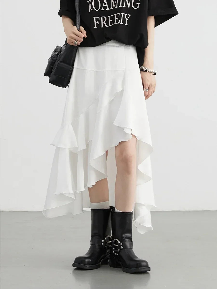 Person wearing a black t-shirt with text, white skirt, and black boots on a plain background