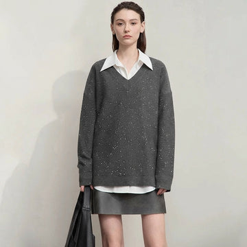 Woman wearing a gray sweater over a white shirt with a plain background