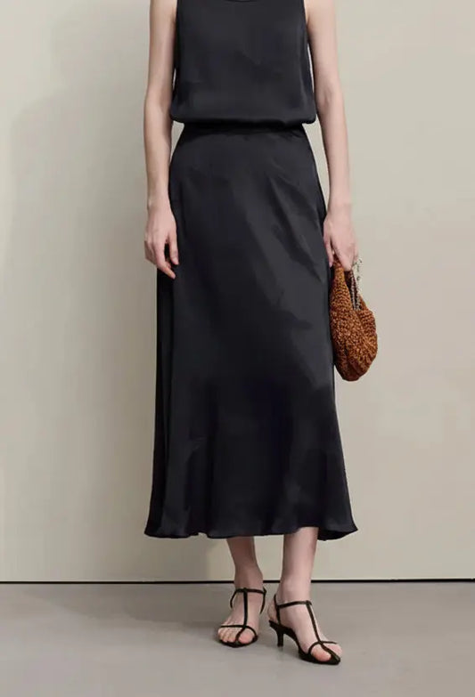 Woman wearing a black dress holding a woven bag against a plain background