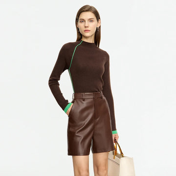 Woman wearing a brown sweater with green trim and leather shorts on a white background