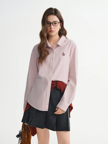 Woman wearing a light pink shirt over a red top with a black pleated skirt on a white background