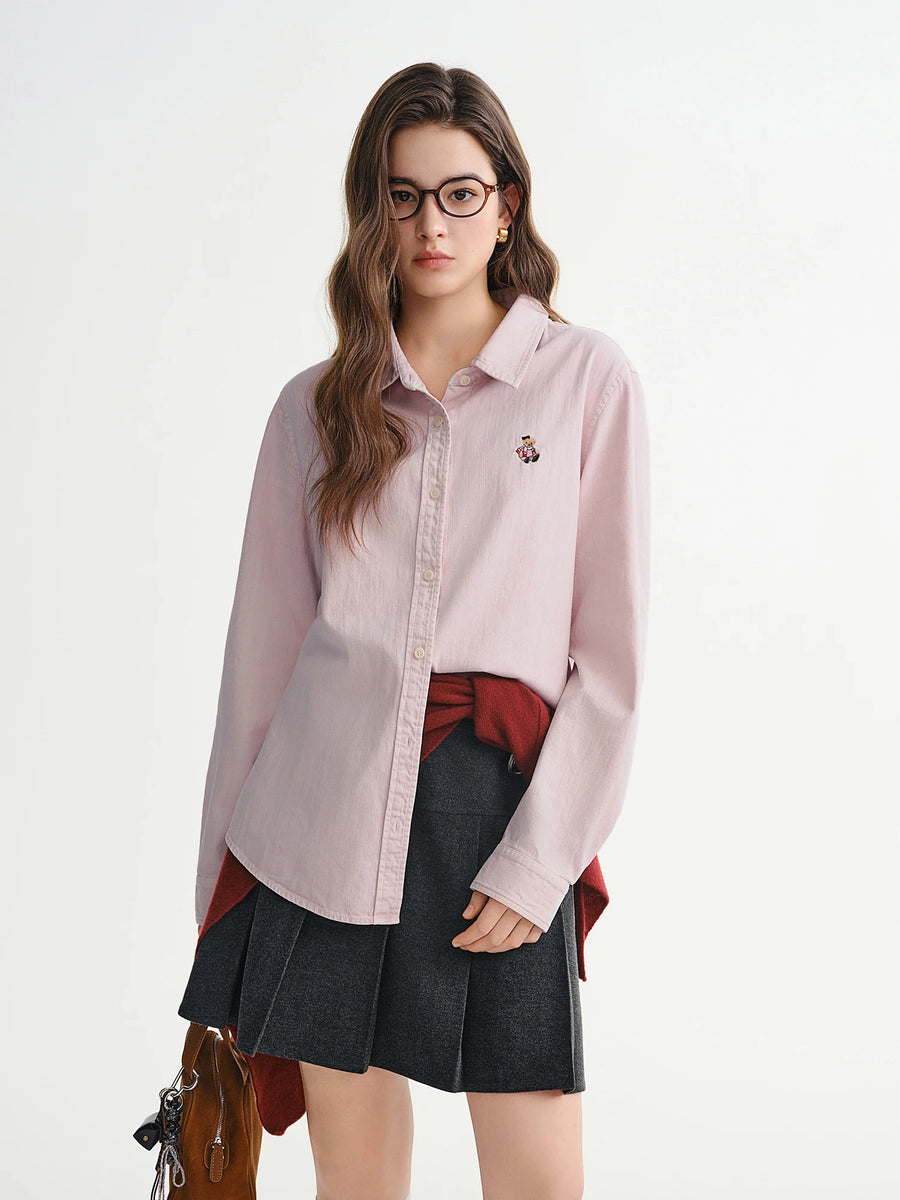 Woman wearing a light pink shirt over a red top with a black pleated skirt on a white background