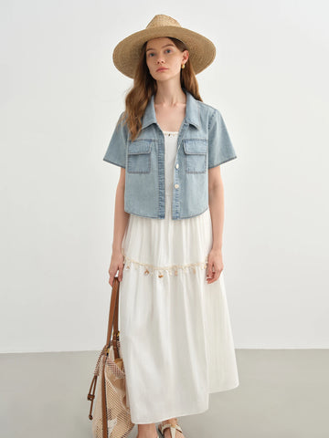 Woman wearing a denim vest over a white dress with a straw hat on a plain background