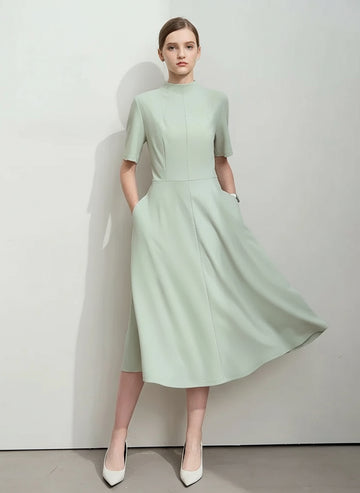 Woman wearing a light green dress with a plain background, featuring the brand 'Amii'.