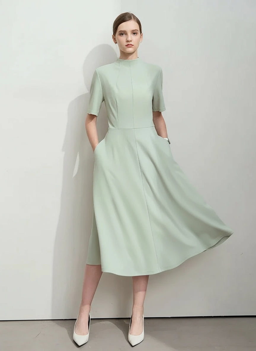 Woman wearing a light green dress with a plain background, featuring the brand 'Amii'.