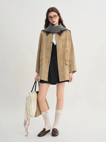 Woman wearing a beige jacket over a black dress with a gray scarf, holding a beige bag.