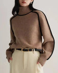 Person wearing a brown sweater with black trim against a plain background