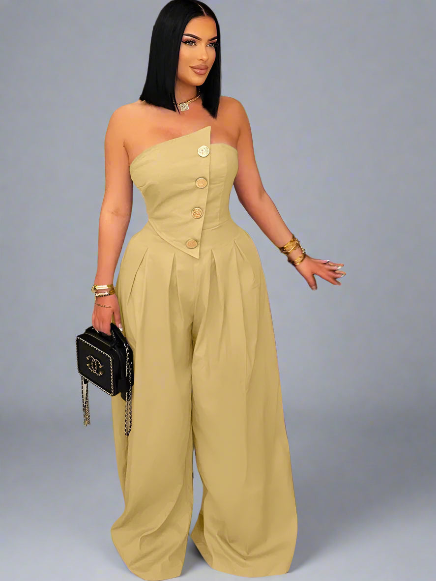 Woman in a beige one-shoulder jumpsuit standing in a room with decorative elements.