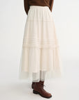Person wearing a white layered skirt with brown shoes on a white background