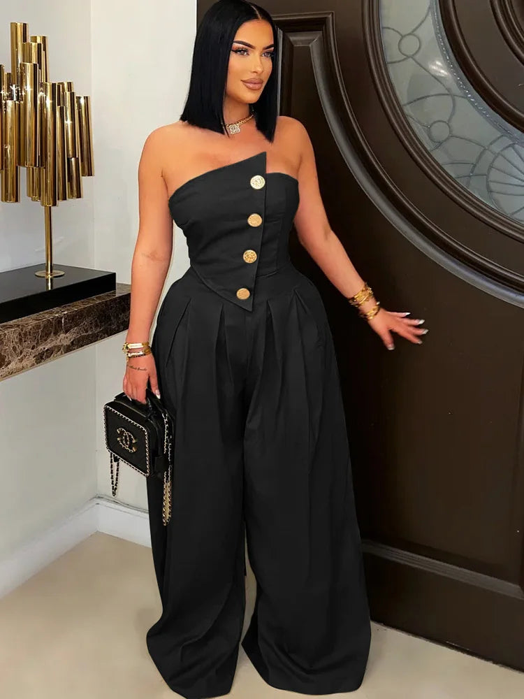 Woman wearing a black one-shoulder jumpsuit with gold buttons, standing indoors.