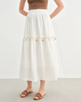 Person wearing a white skirt with decorative trim on a plain background