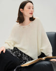 Woman wearing a white sweater sitting with an open book on a gray background