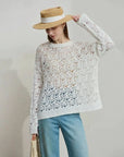 Woman wearing a lace sweater and straw hat with a plain background