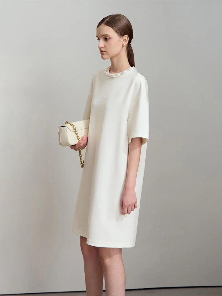 Woman wearing a white dress holding a gold handbag against a plain background