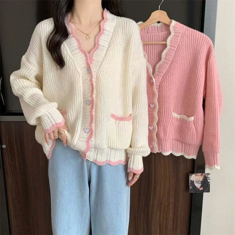 Woman wearing a cream cardigan with pink trim, standing next to a pink cardigan on a hanger.