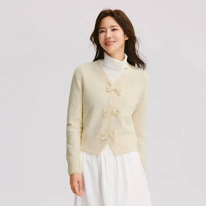 Woman wearing a light yellow cardigan with bow details on a plain background