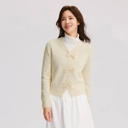 Woman wearing a light yellow cardigan with bow details on a plain background