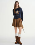 Woman wearing a navy sweater with a floral design, brown skirt, white socks, and brown boots on a white background
