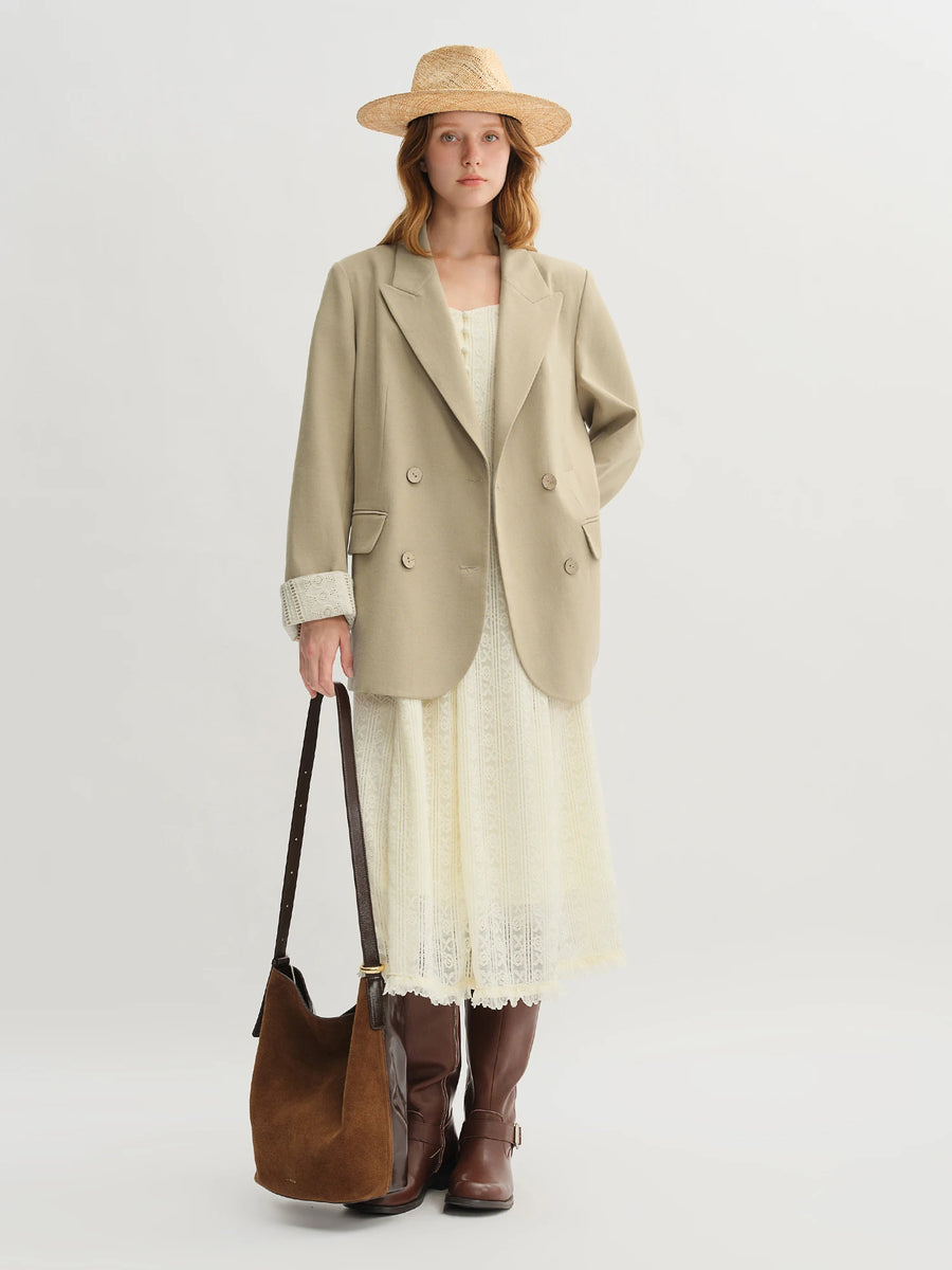 Woman wearing a beige blazer, white dress, brown boots, and straw hat on a white background