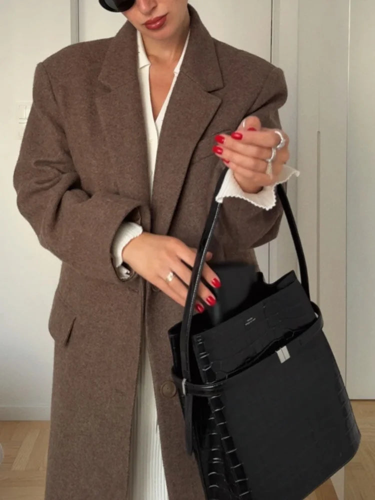 Person wearing a brown coat holding a black handbag indoors.
