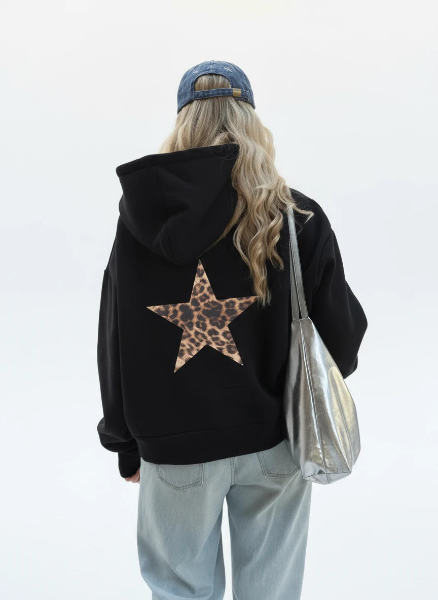 Person wearing a black hoodie with a leopard print star on the back, walking on a street.