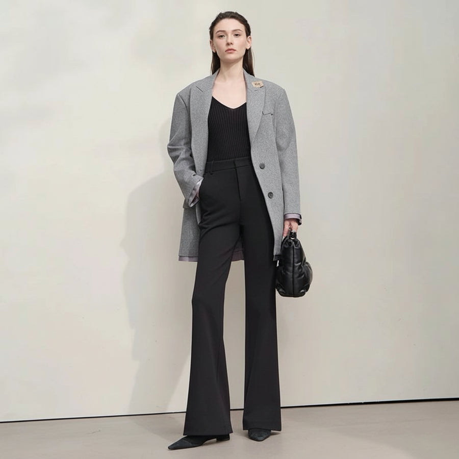 Woman wearing a gray coat and black pants with a black handbag on a plain background, featuring the brand 'Amii'.