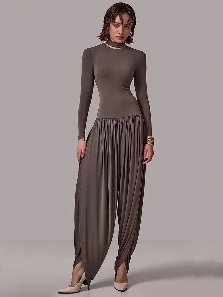 Woman wearing a long-sleeve brown top and flowing pants on a plain background