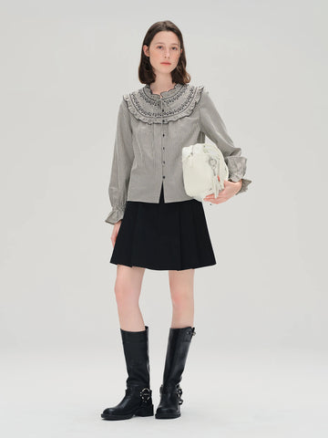 Woman wearing a gray shirt with a ruffled collar, black skirt, and black boots on a white background