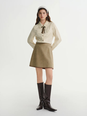 Woman wearing a striped shirt, beige skirt, and black boots on a white background
