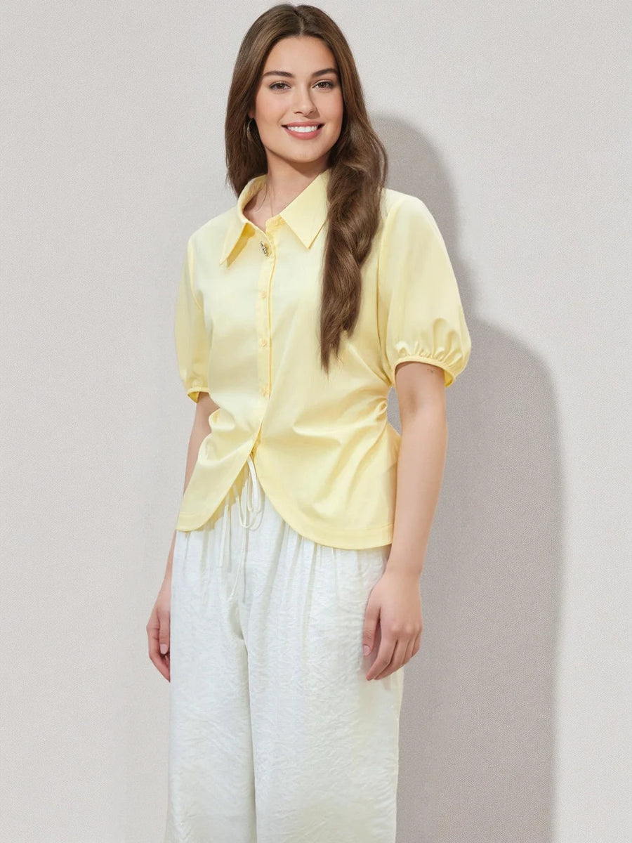 Woman wearing a yellow shirt and white pants against a plain background